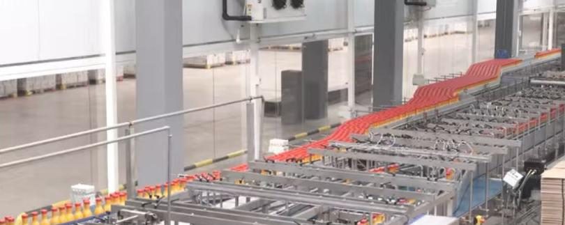 Bottling line with red-capped bottles moving between conveyors